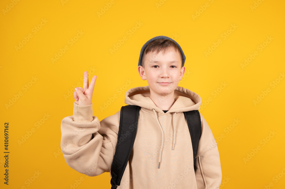 Caucasian boy showing v-sign at the yellow studio free space. Boy in hoodie and hat smiling Caucasian boy showing v-sign at the yellow studio free space. Boy in hoodie and hat smiling