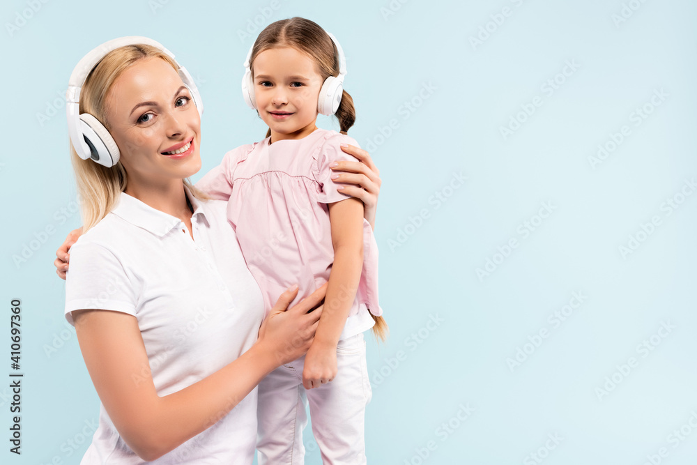 happy mother in wireless headphones holding in arms child isolated on blue happy mother in wireless headphones holding in arms child isolated on blue