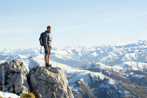 young mountaineer poses in the snow on the edge of a cliff with the mountains in the background in a very dangerous and impressive environment