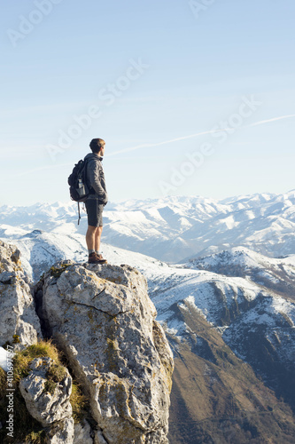 young mountaineer poses in the snow on the edge of a cliff with the mountains in the background in a very dangerous and impressive environment