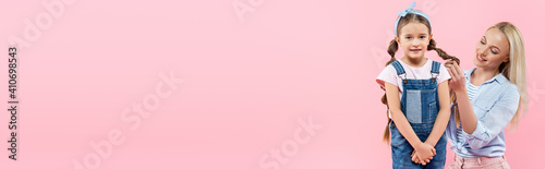 cheerful mother braiding hair of daughter isolated on pink, banner