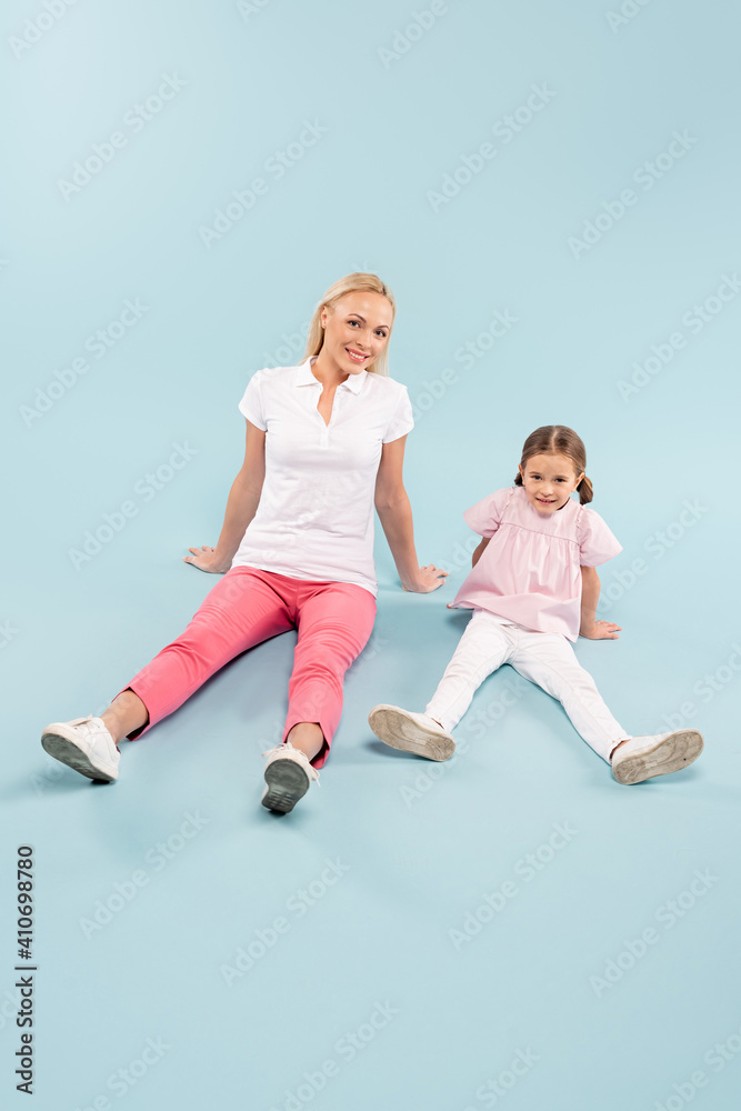 full length of happy mother and kid sitting on blue full length of happy mother and kid sitting on blue