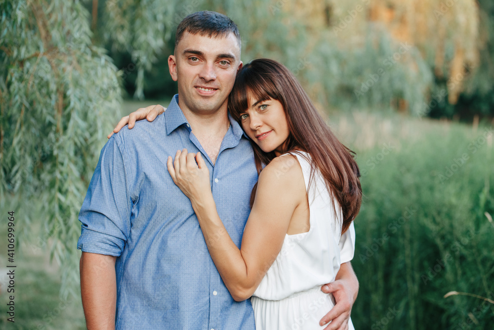 Obraz premium Beautiful married couple man woman in love. Husband and wife hugging in park on summer day at sunset. Togetherness and happiness. Authentic real people family outdoors.