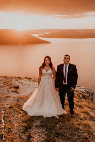 wedding newlyweds in a white dress and suit walk in the summer on the mountain above the river.