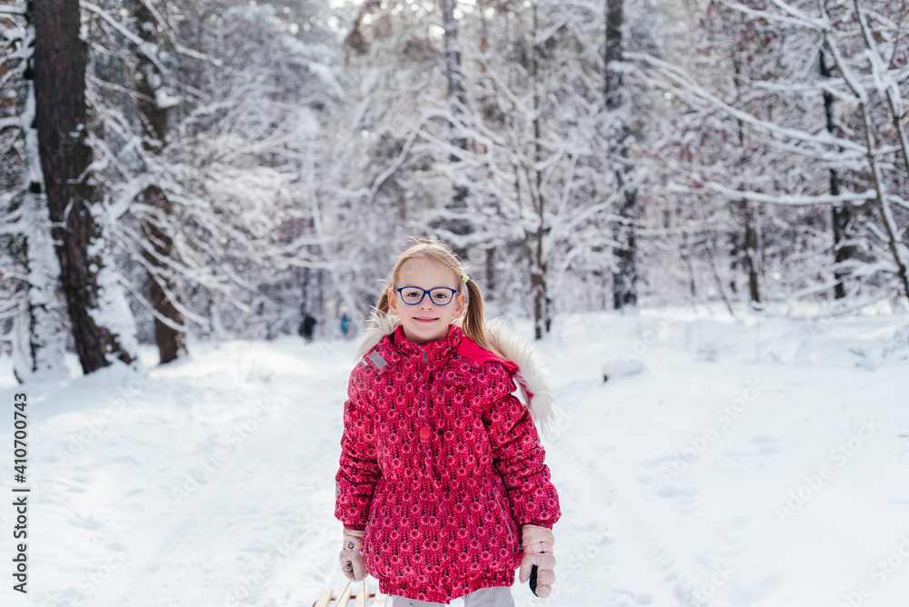 Little girl in eyeglasses pulls sled through beautiful winter forest Little girl in eyeglasses pulls sled through beautiful winter forest