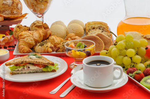 Gastronomy. Breakfast table with cup of coffee, sandwich, fruits, juice jar, fruits and various breads with red tablecloth.