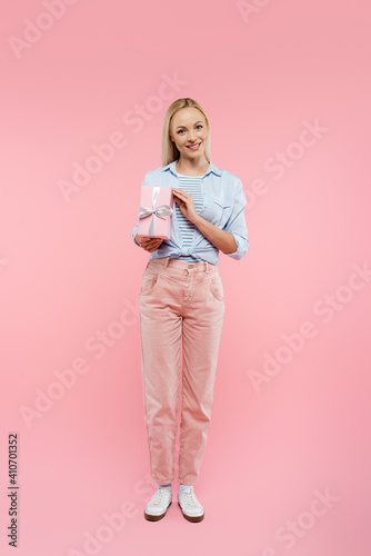 full length of happy woman smiling and holding present on pink