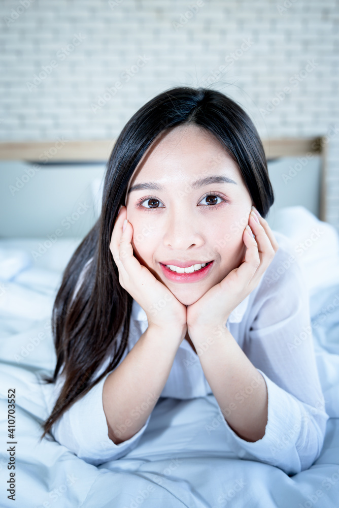 Portrait images of attractive Asian woman Lie down and rest on the white bed, In her bedroom which happily, to people and stay at home concept Portrait images of attractive Asian woman Lie down and rest on the white bed, In her bedroom which happily, to people and stay at home concept