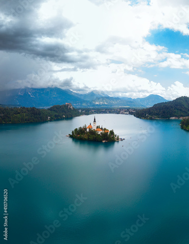 Aerial vertical view of Lake Bled. Cloudy weather, heavy thunderstorm clouds on the horizon. Summer day. Season of tour and travel. Church of the Mother of God, Slovenia, Europe