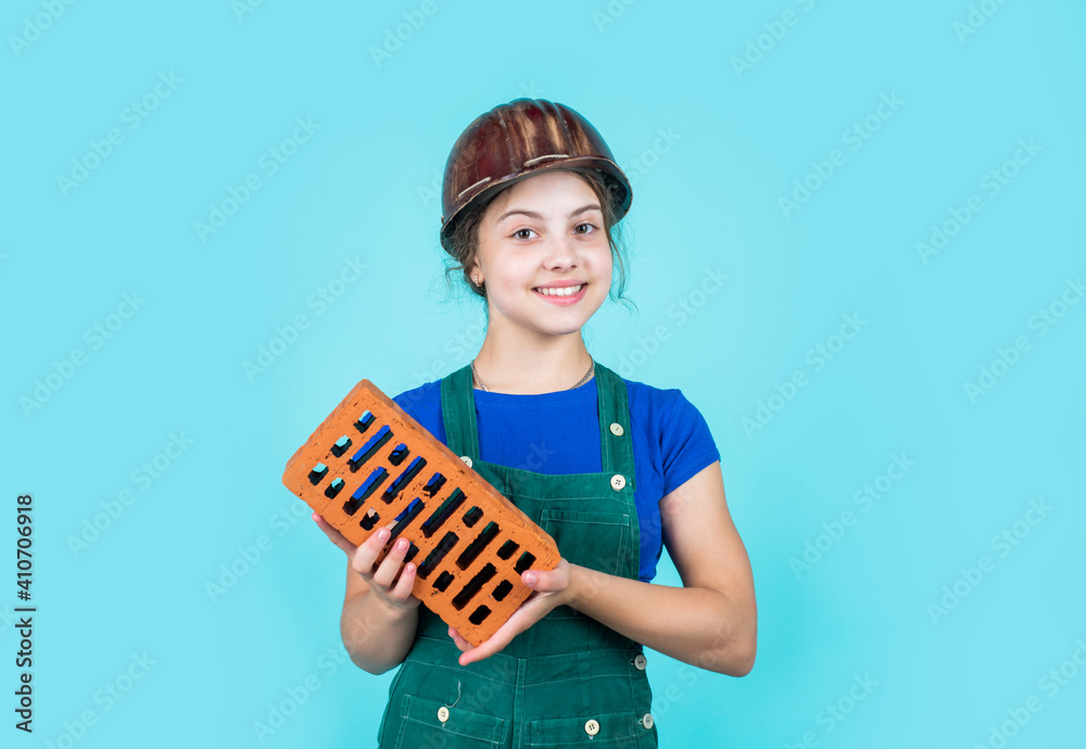 Child in uniform working around brick wall. labour day concept. Little girl bricklayer. learning how to build. Little worker in helmet building from brick. Architecture construction child. Repair Child in uniform working around brick wall. labour day concept. Little girl bricklayer. learning how to build. Little worker in helmet building from brick. Architecture construction child. Repair