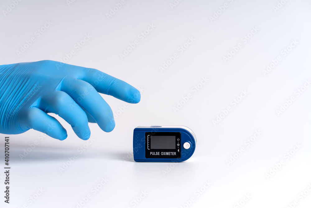 Pulse oximeter on a white background. A hand in a medical glove holds a device for health diagnostics Pulse oximeter on a white background. A hand in a medical glove holds a device for health diagnostics