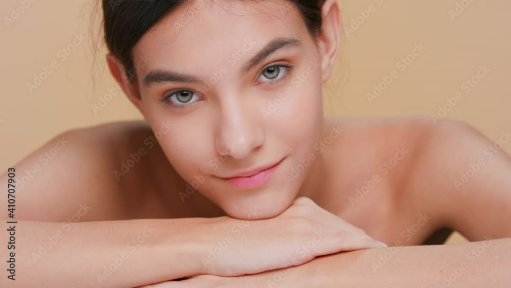Beauty portrait of young brown-haired woman with perfect skin, who slowly puts her chin down on her forearms, looks at camera and smiles | Skin care and beauty product promotional concept Beauty portrait of young brown-haired woman with perfect skin, who slowly puts her chin down on her forearms, looks at camera and smiles | Skin care and beauty product promotional concept