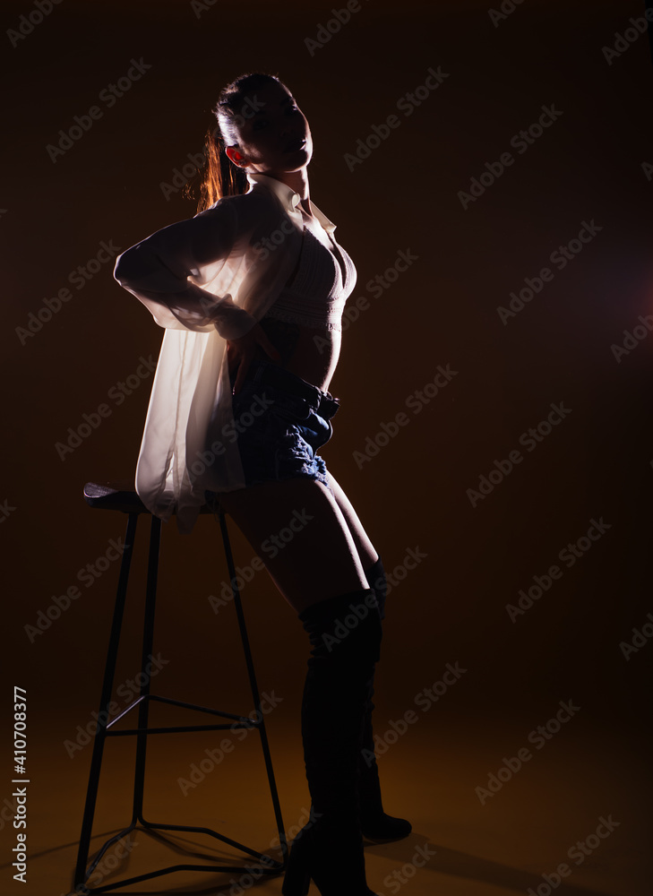 Full-length silhouette portrait on a dark background of a sensational woman posing with a high chair