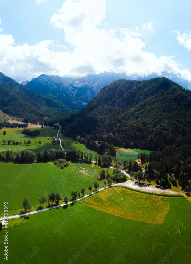 Aerial view over green meadow in Zgornje Jezersko, to Kamnik-Savinja Alps on a sunny summer day in Slovenia. Travel and tourism. Vertical photo