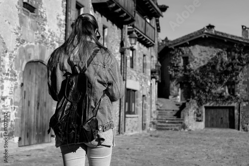 Young woman walking with fashion jeans jacket and backpack in old medieval village.Back view ,black and white photography ,travel and tourism concept with copy space.