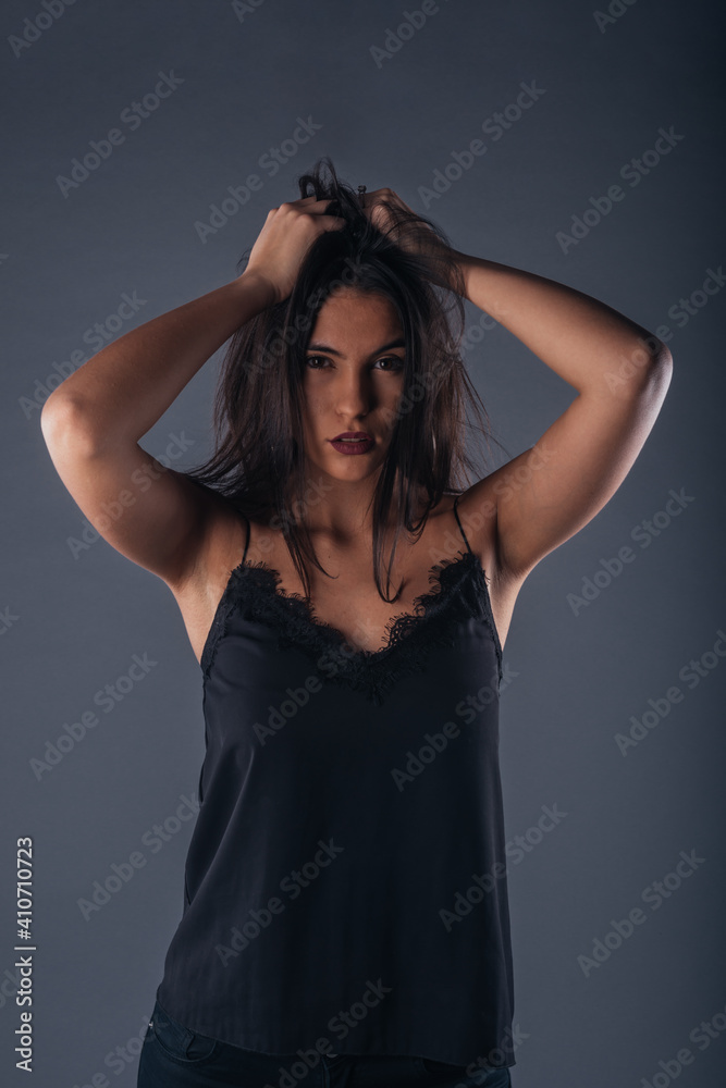 Fototapeta premium Portrait of a beautiful female model looking serious at the camera while touching her brunette hair