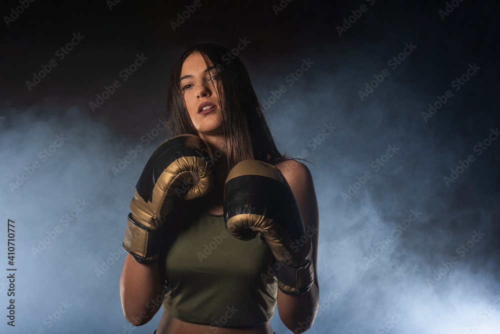 Closeup portrait of a female boxer posing with boxing gloves and looking at the camera with a smokey background