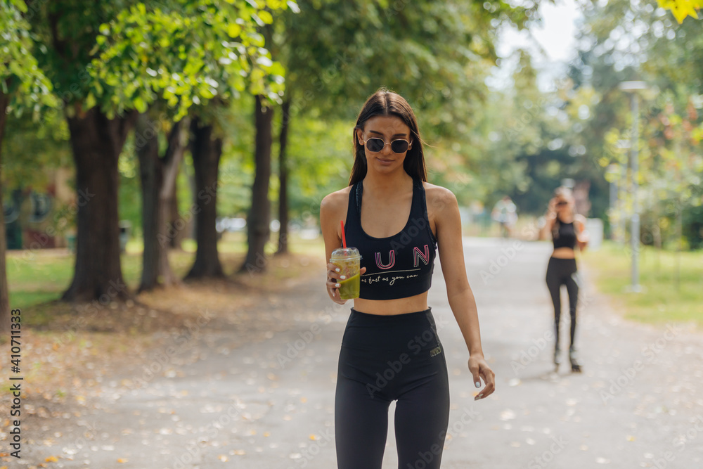 Two women in sportswear rollerblading at the park in sunny weather.. Two women in sportswear rollerblading at the park in sunny weather..