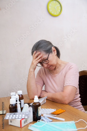 Sad mature woman with  pile of medicines on  table