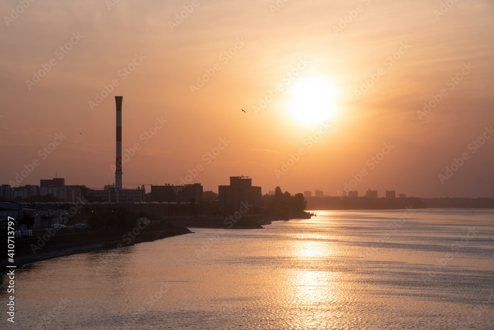 View of the Danube river and the city of Belgrade from Pancevo Bridge (Pančevački most) at sunset. Orange sky and clouds in background.