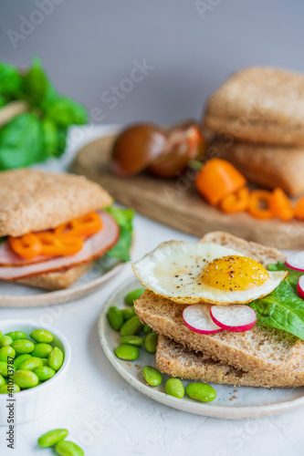 Healthy sandwiches or burgers with whole grains bread, microgreens, egg, fresh vegetables Ketogenic diet, intermittent fasting, weight loss. Breakfast and dieting time concept. White table, copy space