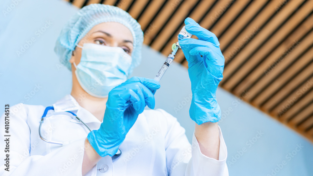 A doctor wearing a protective medical mask prepares to inject with the coronavirus vaccine. The concept of home treatment, calling doctor at home. A doctor wearing a protective medical mask prepares to inject with the coronavirus vaccine. The concept of home treatment, calling doctor at home.