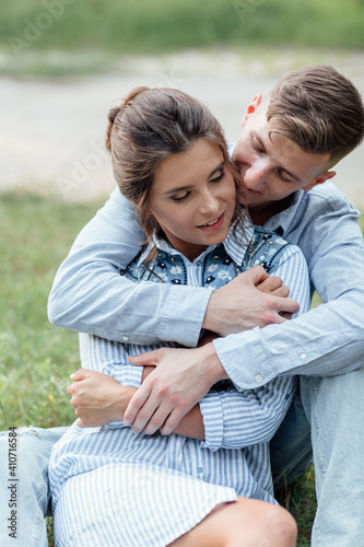 Outdoor shot of young happy couple in love sitting on grass on nature. Man and woman hugging, sunlight in summer park. Happy family in the evening sun light. The concept holiday © Andriy Medvediuk