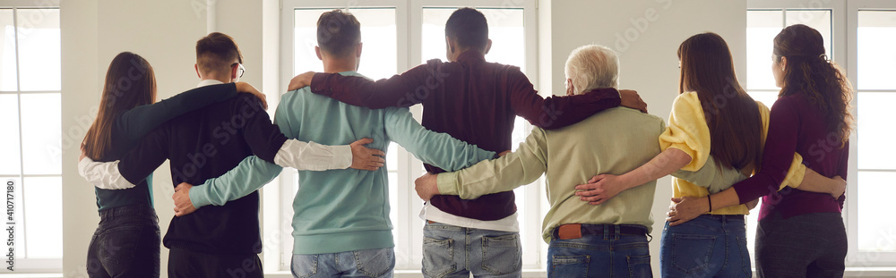 Φωτογραφία Team of people hug standing in a row with their backs to the camera and looking out the window