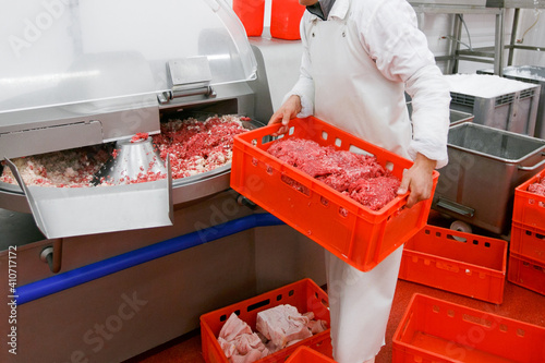 Cropped image of a worker at the meat processing factory, adds spices to minced meat in a processing machine. photo