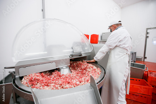 Frame view of a worker at the meat processing factory, adds spices to minced meat in a processing machine. photo