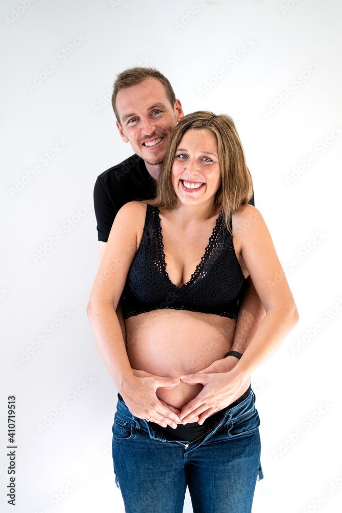 Portrait of young pregnant couple smiling happy putting their hands together in a heart shape on top of their belly Portrait of young pregnant couple smiling happy putting their hands together in a heart shape on top of their belly