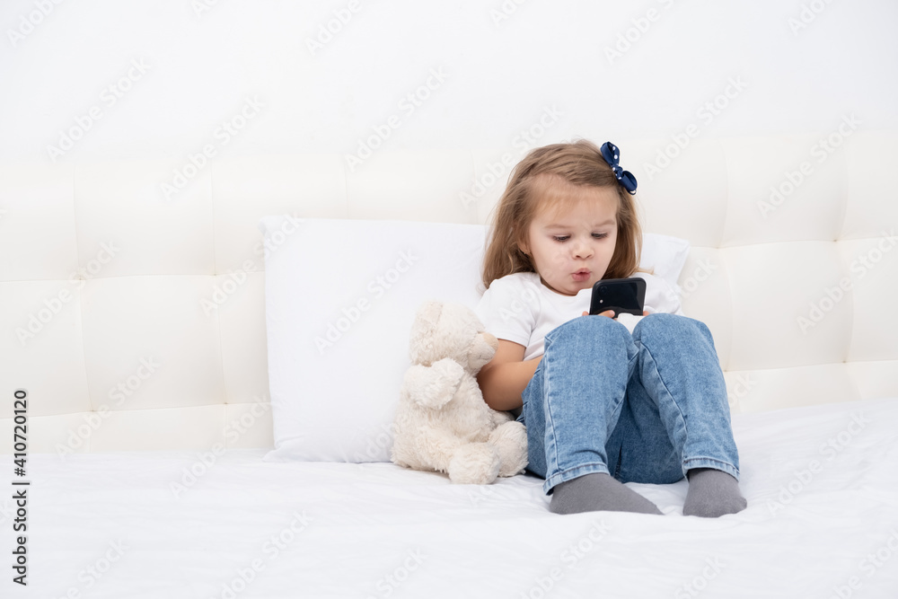 Little girl with hand in cast sitting in bed using smartphone, watching cartoon or education video