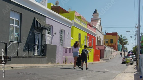 Woman walking with son and baby stroller in the streets of colorful buildings neighbourhood Bo-Kaap Cape Town South Africa.
