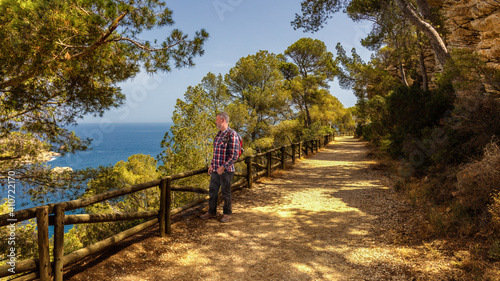 Fototapeta Naklejka Na Ścianę i Meble -  A backpacker hiker walks on a hiking trail on the steep coast near Javea in Spain. He stops and looks out over the Mediterranean. Below are small rock islands in the sea.