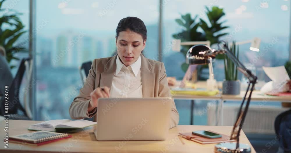 Young Caucasian Office Executive Woman Using Laptop and Writing Work project Designing Plan in Corporate Coworking Shared Workspace. Young Caucasian Office Executive Woman Using Laptop and Writing Work project Designing Plan in Corporate Coworking Shared Workspace.