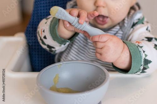 7 month old baby learning to use a spoon to eat applesauce; 2 hands grasp spoon baby led weaning style