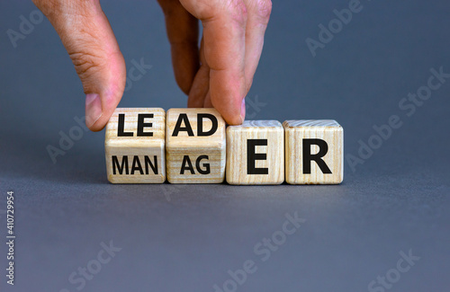 Manager versus leader symbol. Businessman flips wooden cubes and changes the word 'manager' to 'leader'. Beautiful grey background, copy space. Business and manager versus leader concept.