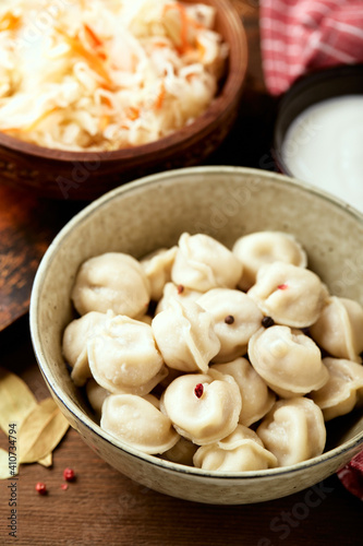 Traditional Russian pelmeni dumplings with sour cream and sauerkraut with sour cream over wooden background. Top view, flat lay.