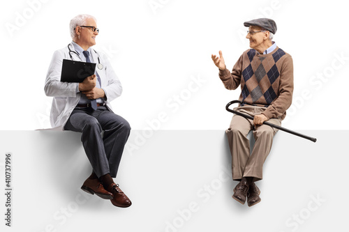 Mature doctor sitting on a blank panel and listening to an elderly male patient