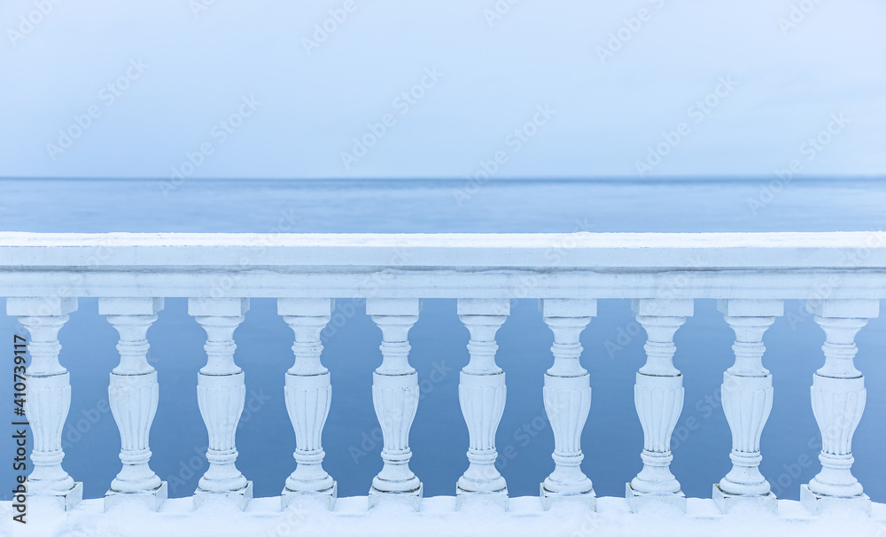 White balcony over winter sea. Snow-covered classic balustrade against the blue sea.