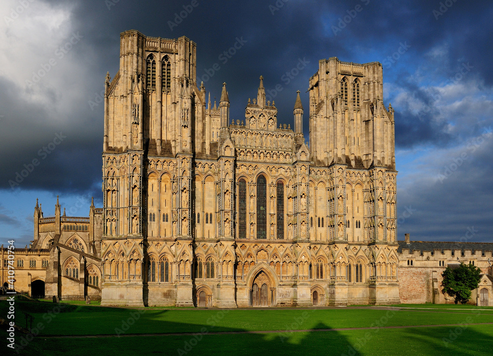 Facade Of St Andrew Cathedral Of Wells England Bathed In Golden Sunlight On A Sunny Summer Day With A Few Dark Clouds In The Sky