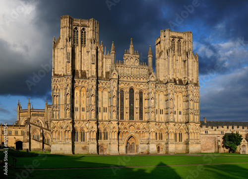 Facade Of St Andrew Cathedral Of Wells England Bathed In Golden Sunlight On A Sunny Summer Day With A Few Dark Clouds In The Sky photo