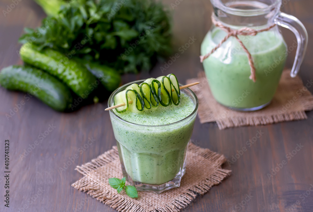 Glass of green cucumber smoothie garnished with cucumber slices on wooden background. Selective focus.