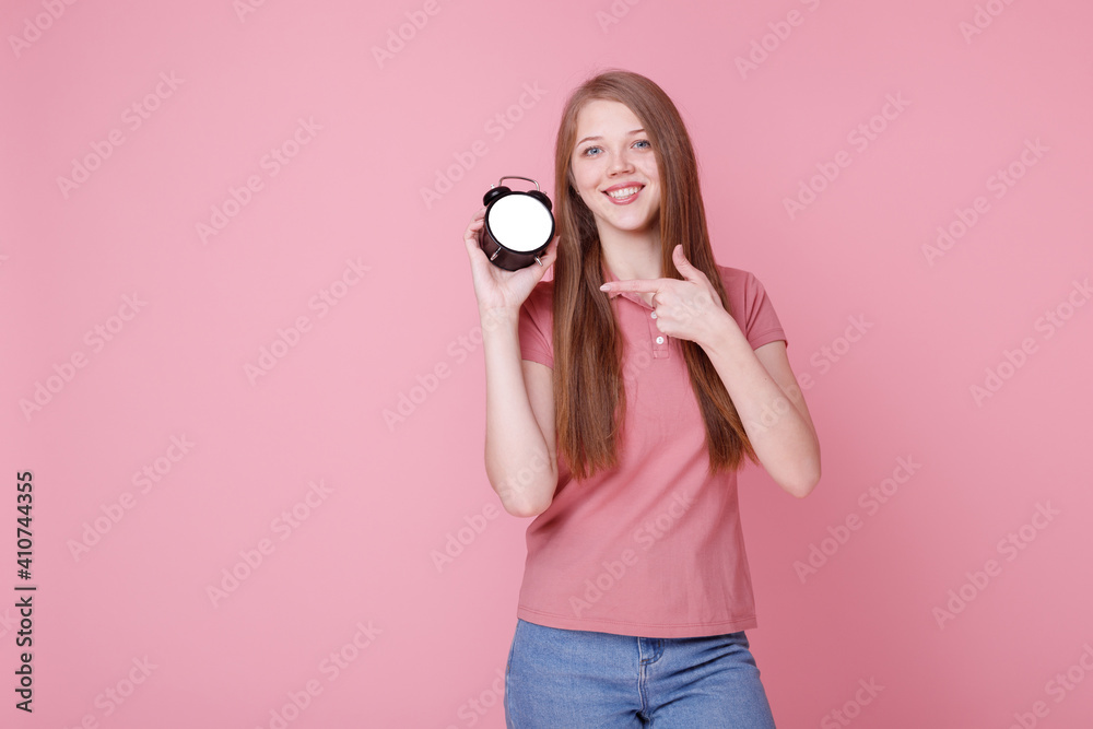 Girl smiles and shows off alarm clock on pink background Girl smiles and shows off alarm clock on pink background