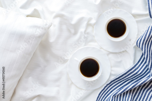 Two cups of coffee on the bed with white linens and blue bedspread . Good morning concept.