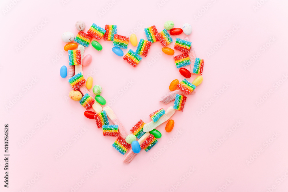 Heart made of colorful sugar candies on a pink background. Valentine's Day concept. Top view, flat lay.