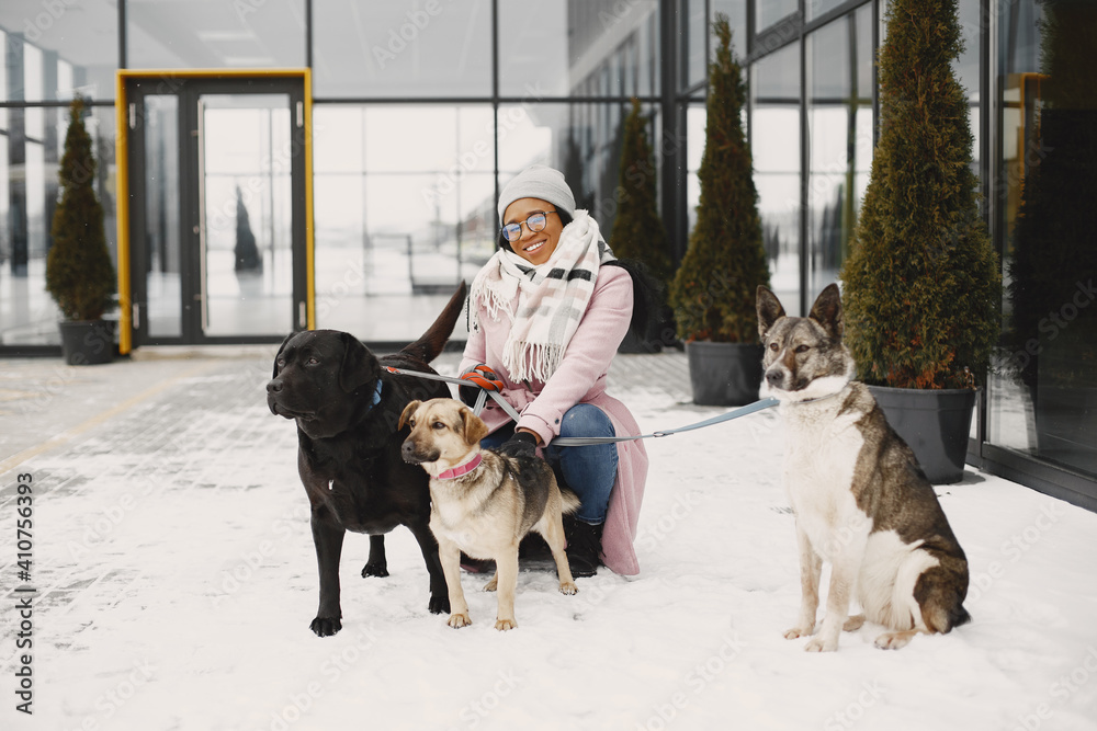 Cute african girl in a winter park. Woman in a pink coat. Walking dogs.