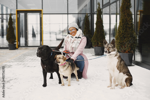 Cute african girl in a winter park. Woman in a pink coat. Walking dogs.