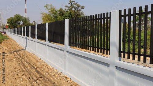 Cement block fence with metal. White cement blocks and black steel lattice fence spans over green plant background and blue sky with copy space. Selective focus