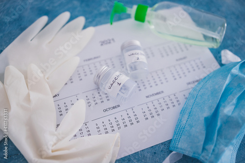 covid-19 vaccine against the pandemic, ampoules with Vaccine 1 and Vaccine 2 labels side by side next to 2021 yearly calendar and gloves mask and sanitizer